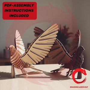 May include: Two wooden bird sculptures with outstretched wings, one light-coloured and one dark-coloured. The birds are on a light-coloured surface. Text in a red box reads "PDF-ASSEMBLY INSTRUCTIONS INCLUDED". The logo "DRAGON LASER CUT" is in the bottom right corner.