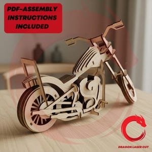 Könnte beinhalten: Ein lasergeschnittenes Motorradmodell aus Holz mit geschichteten hellen Holzpaneelen, einem detaillierten Rahmen, Rädern und Lenker. Ein roter Kasten enthält den Text PDF-ASSEMBLY INSTRUCTIONS INCLUDED und ein rotes Drachenlogo ist zu sehen.