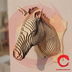 Puede incluir: Decoración de pared con forma de cabeza de cebra de madera, elaborada con capas de madera. La cabeza de cebra es de color marrón claro con rayas marrones oscuras, montada sobre una placa de madera marrón claro. Diseño moderno y artístico.