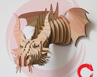 May include: A three-dimensional wall-mounted dragon head sculpture constructed from layered light brown wood pieces. The design features intricate laser-cut details, prominent horns, and extended wings. A red circular logo with the text DRAGON LASER CUT.