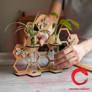 May include: Wooden honeycomb-shaped plant holder with three clear glass test tubes for displaying small plants. The holder features decorative bee cutouts and is made of light-colored wood. The plants have green leaves and are in water.
