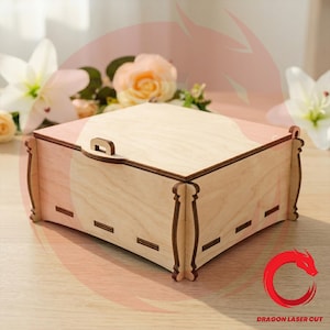 Puede incluir: Una caja cuadrada de madera con tapa plana y un pequeño cierre, que presenta paneles de madera clara con detalles cortados con láser de bordes oscuros en las esquinas y los lados. La caja tiene una superficie superior lisa.