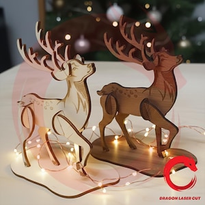 May include: Two laser-cut wooden deer figures standing on individual oval bases. One deer is light-colored wood, and the other is a darker brown wood. Both feature intricate antler designs and are surrounded by thin, glowing string lights.