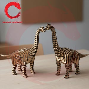 May include: Two laser-cut wooden Brachiosaurus dinosaur models with a layered design. The dinosaurs are facing each other, their necks touching. The models are light brown and stand on a light-coloured surface. The text "DRAGON LASER CUT" is in the upper left corner.