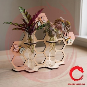 May include: A wooden honeycomb-shaped plant holder with three glass test tubes, each holding a small plant. The holder features decorative wooden bees and is made of light-colored wood. The plants have green and burgundy leaves.