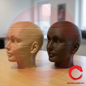 May include: Two wooden human head sculptures, one light-colored and the other dark brown. The heads are constructed from layered horizontal pieces, creating a unique, textured appearance. The sculptures are displayed on a light-colored wooden surface.