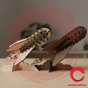 May include: Two laser-cut wooden rocket ship sculptures, one in light wood and one in dark wood, featuring a skeletal frame design with flame-shaped bases. The text DRAGON LASER CUT is visible in the bottom right corner of the image.