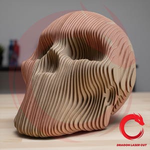 Puede incluir: Una escultura de calavera de madera con un diseño en capas. La calavera está hecha de madera de color marrón claro con un tono marrón rojizo en la parte superior. La escultura tiene una forma suave y curvada y está diseñada con líneas horizontales.
