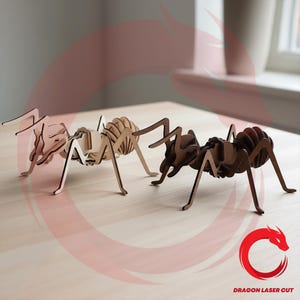 Puede incluir: Tres esculturas de hormigas de madera en tonos marrones y beige se exhiben sobre una superficie de madera clara. Las hormigas están intrincadamente diseñadas, con cuerpos segmentados y patas detalladas, mostrando una estética cortada con láser. Las esculturas están posicionadas para sugerir movimiento.