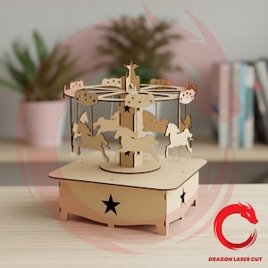 May include: A light-coloured wooden carousel model featuring a central pillar topped with a star, surrounded by several horse figures suspended from a circular frame. The base is square with cut-out star shapes on each side and a smooth flat top.
