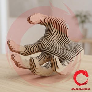 May include: A wooden sculpture of a hand, crafted from layered, light-colored wood with dark lines. The hand is in an open position, with fingers slightly curved. The design is intricate and modern, with the text "DRAGON LASER CUT" and a red dragon logo.