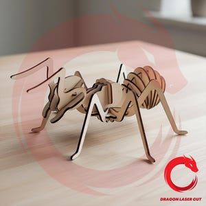 May include: A light brown wooden ant model constructed from interlocking laser-cut pieces. The insect figure features a segmented body, thin legs, and long antennae. A red circular logo with a dragon graphic and the text DRAGON LASER CUT is visible.