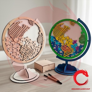 Peut inclure: Deux globes circulaires en bois avec des continents découpés au laser et de petites pièces en forme de croix. Un globe est en bois clair, l'autre a un cadre vert, une base bleue et des continents multicolores. Une boîte en bois et deux stylos.