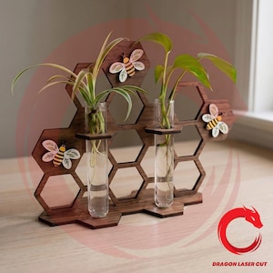 May include: A wooden honeycomb-shaped plant holder with three clear glass test tubes, each holding a small plant. Decorative wooden bees are attached to the honeycomb. The wood is a dark brown color.