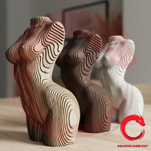Puede incluir: Tres esculturas de madera de un torso femenino en diferentes tonos de marrón y blanco. Las esculturas están hechas de madera en capas, creando un efecto contorneado. Las esculturas se exhiben sobre una superficie de madera de color claro.