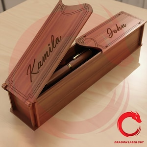 Può includere: Un astuccio per penne in legno con il coperchio aperto, che rivela una penna all'interno. La scatola è incisa con i nomi "Kamila" sul coperchio e "John" sulla parte superiore. La penna ha una clip e dettagli dorati. La scatola è in legno marrone rossiccio.