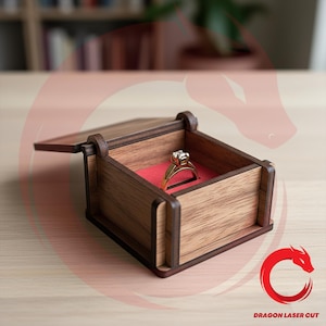 Puede incluir: Un joyero de madera con tapa con bisagras, que muestra un anillo de oro con un diamante. El interior está forrado con tela roja. La caja está hecha de madera marrón claro con ribetes marrones oscuros.