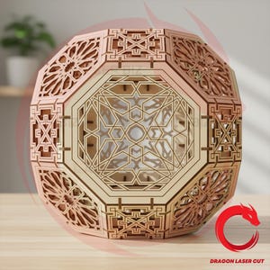 Può includere: Una lanterna geometrica in legno con intricati motivi tagliati al laser. Il design sfaccettato presenta pannelli traforati con forme a stella e geometriche. La lanterna è realizzata in legno chiaro e poggia su una superficie di legno. Il testo "DRAGON LASER CUT" è visibile.