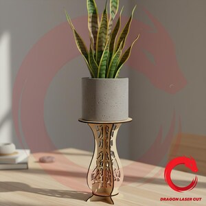 Puede incluir: Un soporte para plantas de madera clara con intrincados patrones cortados con láser, que sostiene una maceta cilíndrica gris moteada con una planta de serpiente verde y amarilla. La base del soporte es acampanada y el texto DRAGON LASER CUT es visible.
