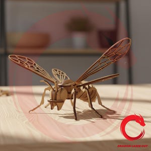 Puede incluir: Modelo de avispa de madera con alas y cuerpo detallados, ensamblado a partir de piezas cortadas con láser. El modelo de insecto es marrón y se encuentra sobre una superficie de madera clara. Las alas tienen un diseño delicado y estampado.