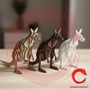 May include: Three standing kangaroo figurines constructed from layered, laser-cut wood pieces. The left kangaroo is light tan, the centre is dark brown, and the right is white. A red dragon logo and the text DRAGON LASER CUT appear in the corner.