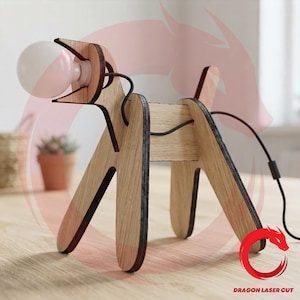 May include: A dog-shaped table lamp constructed from light-colored wood panels with dark edges. The lamp features a spherical white light bulb held in the dog's mouth, with a black power cord running along the back and extending from the rear.