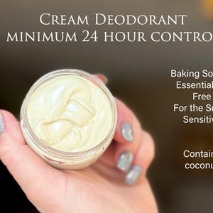 May include: A jar of cream deodorant held in a hand. The cream is a light yellow color. Text on the image reads "Cream Deodorant Minimum 24 Hour Control" and "Baking Soda & Essential Oil Free For the Super Sensitive Contains coconut."