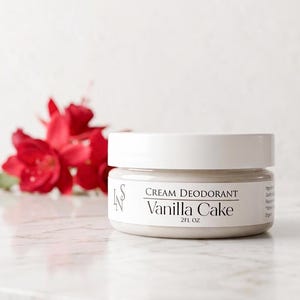 Könnte beinhalten: Ein runder weißer Tiegel mit Deocreme, beschriftet mit Vanilla Cake und einer Füllmenge von 2FL OZ. Das Etikett zeigt den Text LNS, Cream Deodorant, Vanilla Cake und 2FL OZ in schwarzer Schrift. Der Tiegel enthält eine hellbeige Creme.