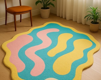 May include: A colorful, abstract rug with a wavy, organic design. The rug features a light blue base with pink and yellow shapes, outlined in yellow. The rug is placed on a wooden floor, and a wooden chair is visible in the background.
