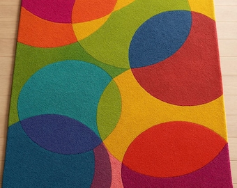 May include: A rectangular area rug with a vibrant, colorful design. Overlapping circles in shades of pink, orange, yellow, green, blue, and red create a bold, abstract pattern. The rug is placed on a light-colored wooden floor.