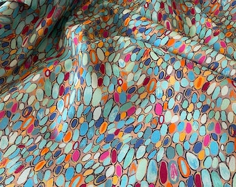 May include: A fabric with a repeating pattern of colorful, oval shapes in shades of blue, teal, pink, orange, and purple. The shapes are outlined in black and set against a tan background. The fabric has a slight sheen.