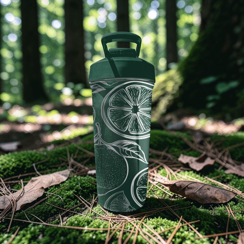 May include: A dark green water bottle with a white citrus fruit design. The bottle has a handle on the lid and is cylindrical in shape. The design includes slices of citrus fruit and leaves. The bottle is set against a natural background of moss and trees.