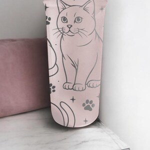 May include: A light pink tumbler featuring a cat illustration, paw prints, and stars. The cat is depicted in a seated position with a detailed outline. The design is repeated on the tumbler's surface, creating a whimsical pattern.