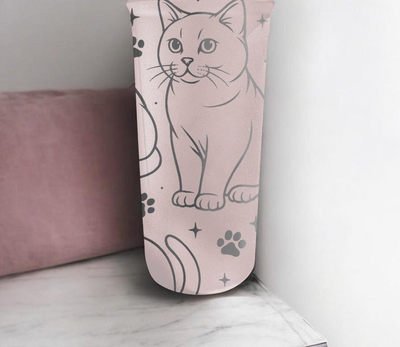May include: A light pink tumbler featuring a cat illustration, paw prints, and stars. The cat is depicted in a seated position with a detailed outline. The design is repeated on the tumbler's surface, creating a whimsical pattern.