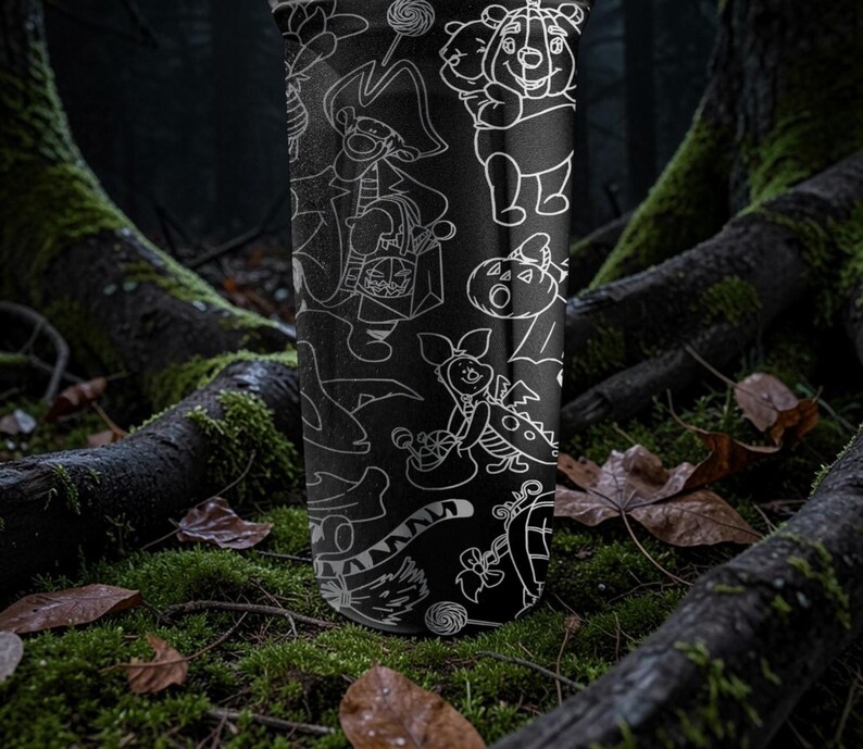 May include: Black tumbler with white line art of cartoon characters in Halloween costumes. The design includes Winnie the Pooh, Piglet, and other characters with candy and pumpkins. The tumbler is set against a forest background with moss and fallen leaves.
