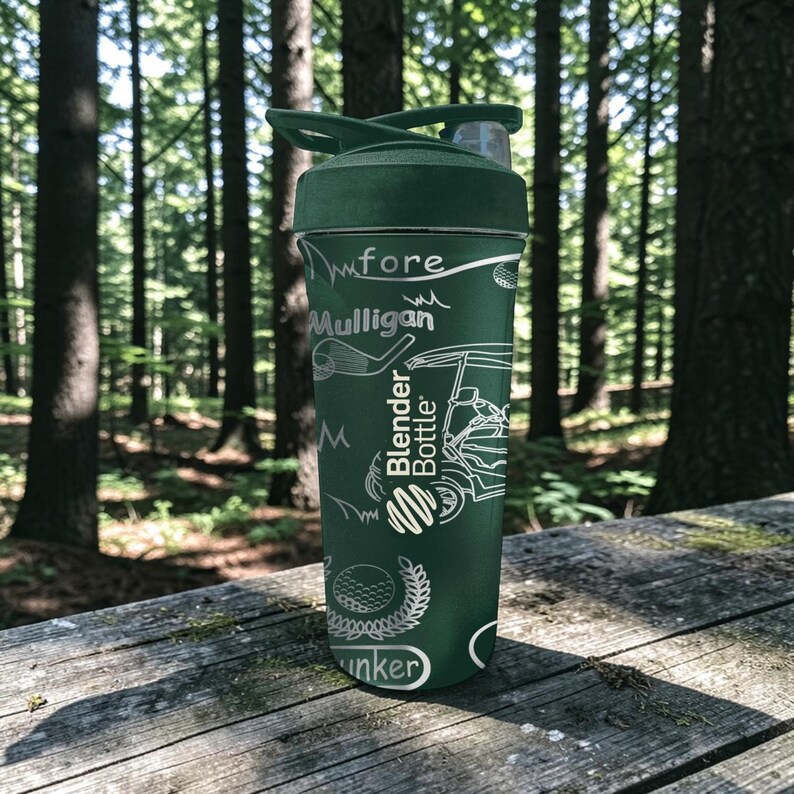 May include: A dark green Blender Bottle with a golf-themed design. The bottle features white illustrations of golf clubs, a golf cart, and a golf ball. The words "fore", "Mulligan", and "Bunker" are also visible on the bottle.