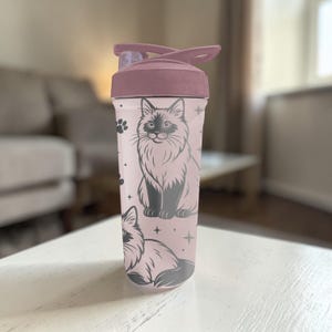 May include: A pink water bottle with a flip-top lid and a black cat illustration. The cat is depicted in a detailed, stylized drawing. The bottle also features paw prints and star accents.
