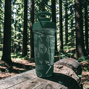 May include: A dark green water bottle with a handle and golf-themed illustrations in white. The bottle features images of a golfer, golf clubs, and other golf-related items. The word "DOGEY" is printed on the bottle.