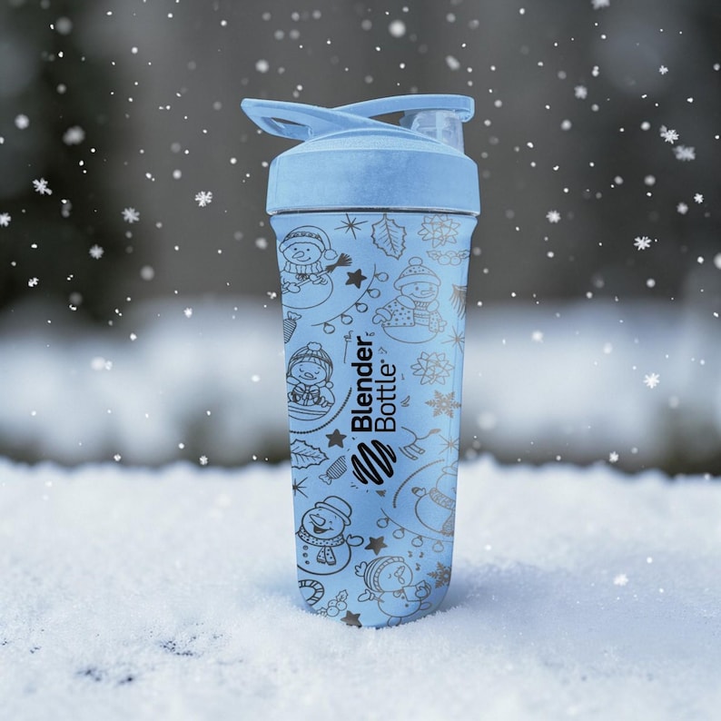 Puede incluir: Una botella Blender Bottle azul claro con tapa abatible. La botella est&aacute; decorada con un patr&oacute;n de invierno de mu&ntilde;ecos de nieve, estrellas y copos de nieve. El logotipo de Blender Bottle es visible en el lateral.