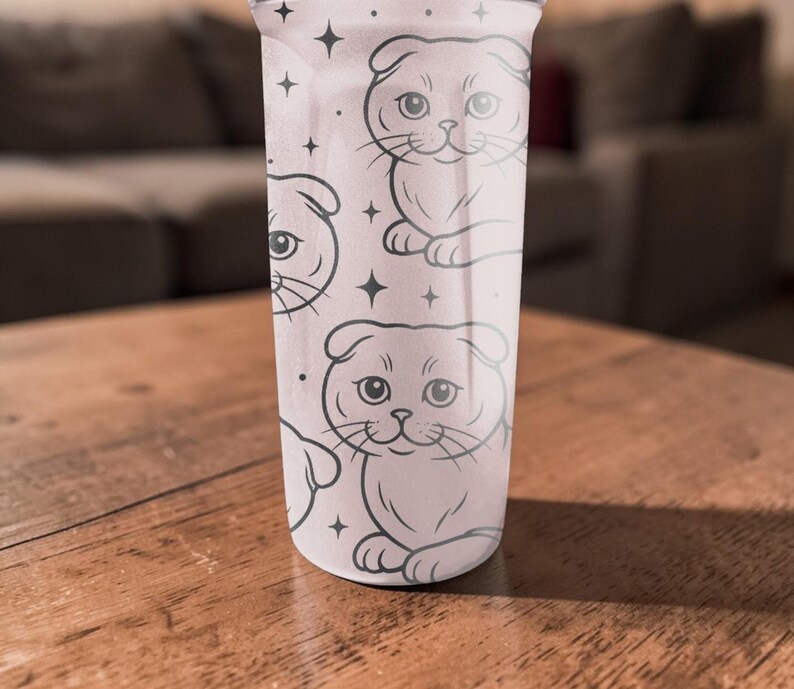 May include: A light pink tumbler featuring a repeating pattern of cartoon Scottish Fold cats in black outline. The cats are in a sitting position with their ears folded. Small black star shapes are scattered around the cats.