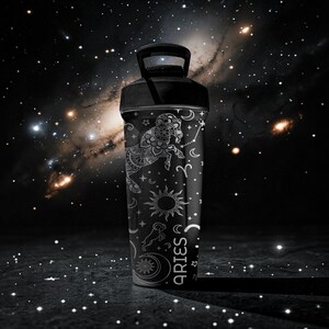 Pode incluir: Garrafa de &aacute;gua preta com tampa preta, com um design branco do zod&iacute;aco de &Aacute;ries. O design inclui um carneiro de &Aacute;ries, constela&ccedil;&otilde;es, s&iacute;mbolos de sol e lua. A palavra "ARIES" &eacute; impressa verticalmente.