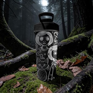 May include: Black water bottle with a black handle and lid. The bottle features a white illustration of a girl with button eyes, a cat, and other characters. The background is a dark forest scene.