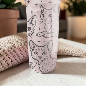 May include: A pink tumbler featuring a repeating pattern of cat illustrations and star accents. The cats are depicted in a detailed, line-art style. The tumbler is made of a clear material and is designed for cold beverages.
