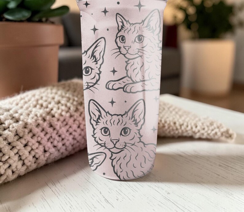 May include: A pink tumbler featuring a repeating pattern of cat illustrations and star accents. The cats are depicted in a detailed, line-art style. The tumbler is made of a clear material and is designed for cold beverages.