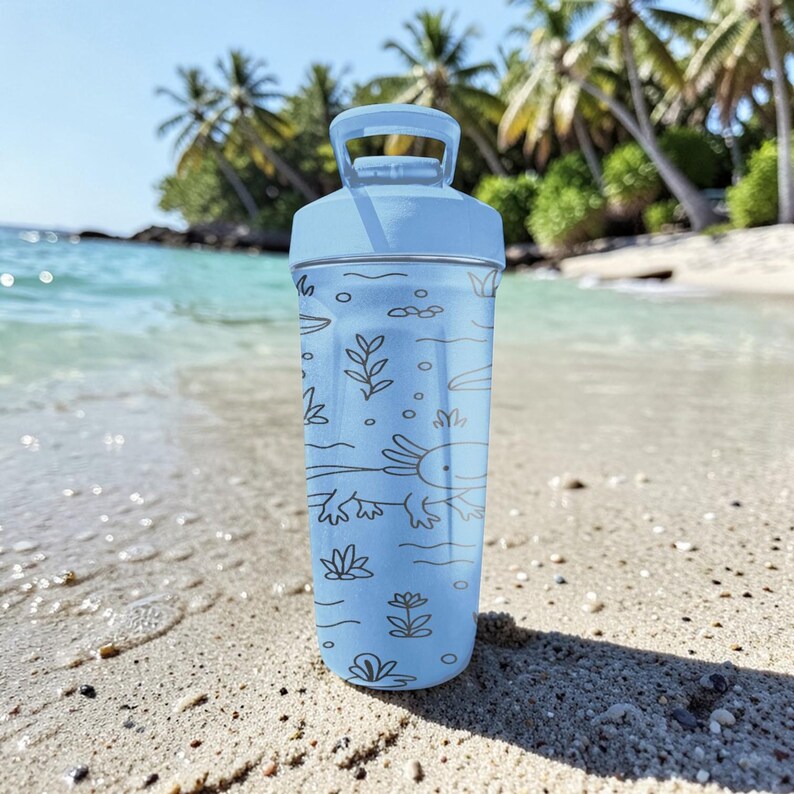 May include: A light blue water bottle with a handle and a screw-on lid. The bottle features a black line drawing of an axolotl and aquatic plants. The bottle is sitting on a sandy beach with palm trees and ocean in the background.