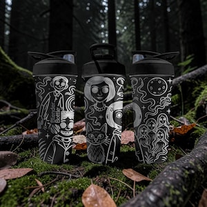 May include: Three black Blender Bottles with white illustrations of characters and designs. One bottle features a character with buttons for eyes, another a girl with a cat, and the third a moon and figures. The bottles are set in a forest.