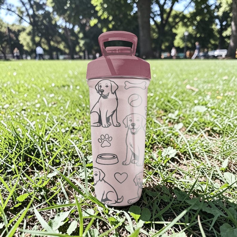 May include: A pink water bottle with a maroon lid and handle. The bottle is decorated with line drawings of dogs, paw prints, a dog bowl, a bone, and a heart. The bottle is sitting on a grassy surface.