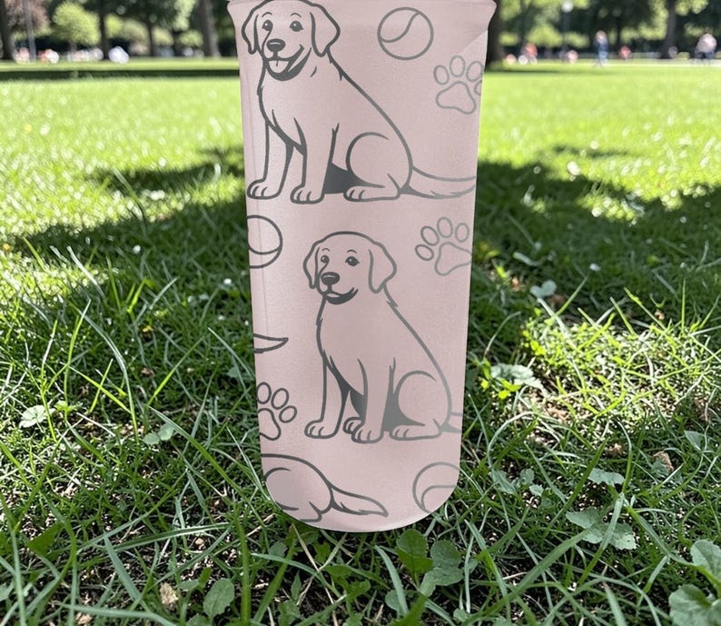 May include: A light pink tumbler with a repeating pattern of a dog, paw prints, and a ball. The dog is light grey and sitting. The cylindrical tumbler appears to be made of plastic.