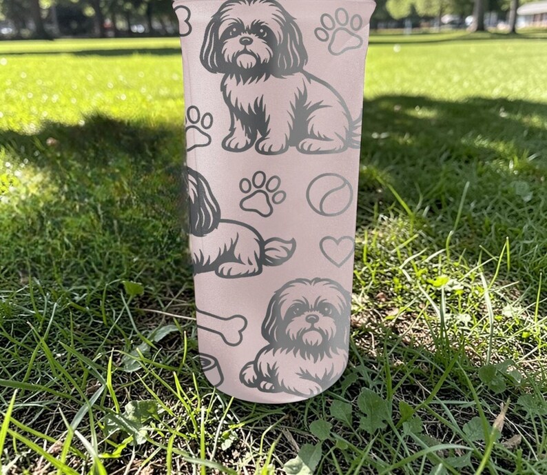 May include: A light pink tumbler featuring a Shih Tzu dog design. The tumbler has multiple illustrations of the dog, paw prints, a bone, a heart, and a ball. The tumbler is sitting on green grass.