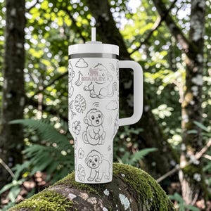 May include: A white stainless steel tumbler with a handle and a straw, featuring a repeating black line art pattern of monkeys, bananas, tropical leaves, and flowers. The Stanley logo is printed in the centre near the top of the vessel.